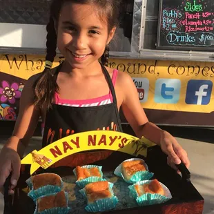 a young girl holding a tray of cupcakes