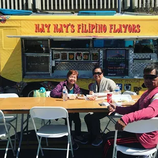 three people sitting at a table in front of a food truck