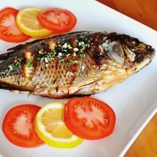 a fish on a plate with tomatoes and lemons