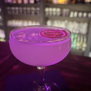 a purple cocktail with a slice of lemon on the rim