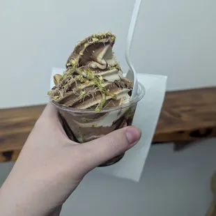 A &quot;bougie&quot; Dubai chocolate and vanilla soft serve in a cup. It is topped with pistachio shavings and syrup.