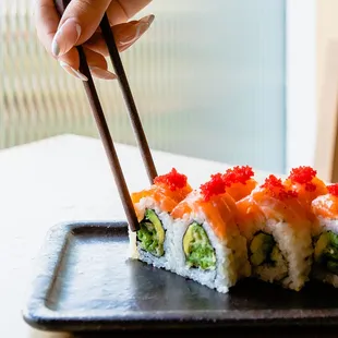 a person holding chopsticks over a plate of sushi