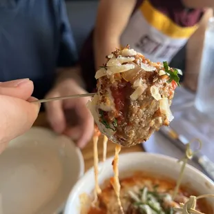 a hand holding a piece of meatball pizza