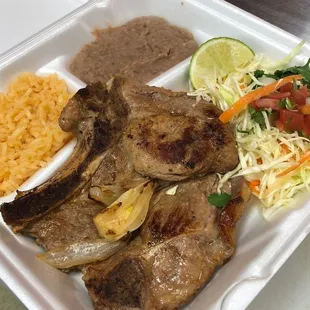 Pork Chop Plate served with a side of rice, refried beans and cabbage mix. Chuleta de Puerco con arroz, frijoles, y ensalada de repollo.