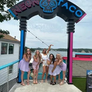 a group of girls posing in front of a neon taco sign