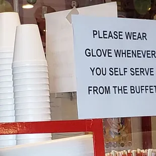 plastic cups and a sign that reads please wear gloves whenever you self serve from the buffet