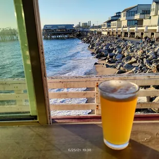 a glass of beer on a table overlooking the ocean
