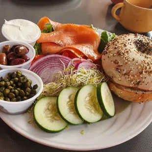 a bagel with salmon, cucumbers, pickles, and olives