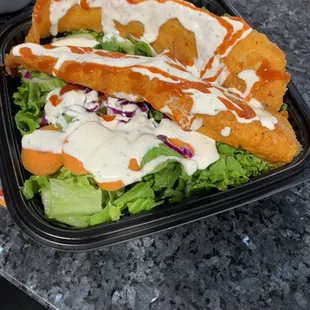 Fish over rice and salad with white and red sauce.