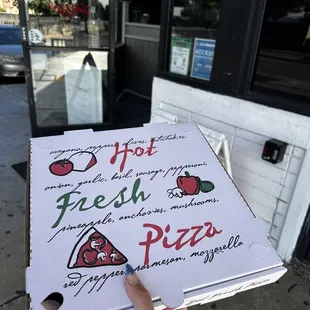 a hand holding a box of fresh pizza