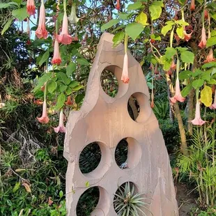 a stone sculpture with pink flowers hanging from it