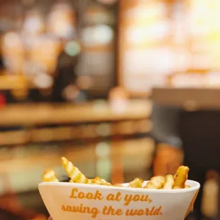 a hand holding a bowl of fries