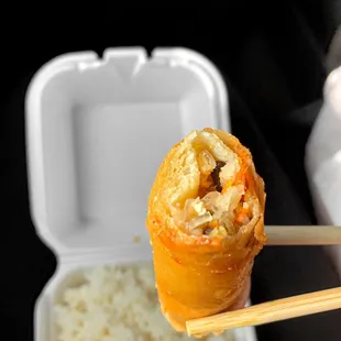 a person holding chopsticks over a container of rice