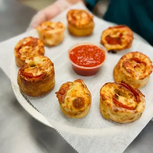 a person holding a plate of mini pizzas