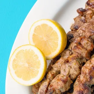 a plate of kebabs with lemon slices