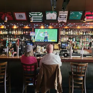 a man and a woman sitting at a bar watching a football game