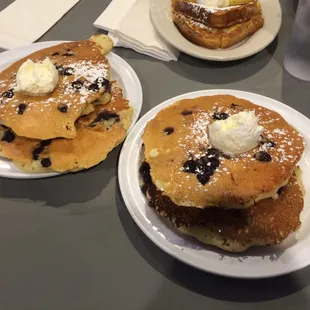 Two sets of blueberry pancakes with powdered sugar and butter on top.