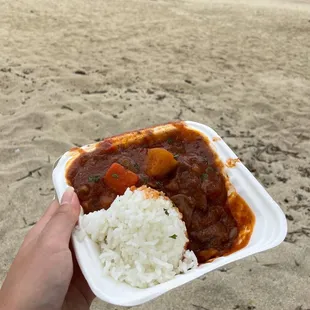 a hand holding a plate of rice and stew
