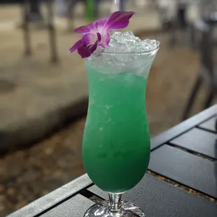 a green cocktail with a purple flower