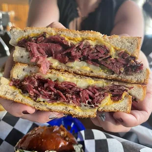 a person holding a sandwich with meat and cheese