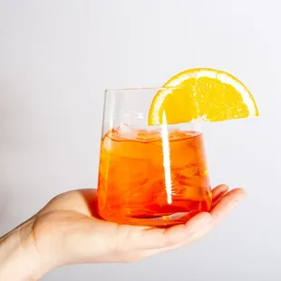 a person holding a drink with a slice of orange