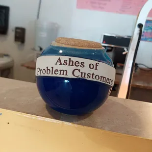a blue vase with a label that says ashes of problem customers