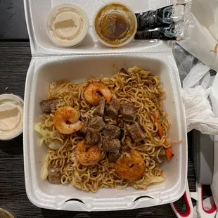a take out box with noodles and shrimp