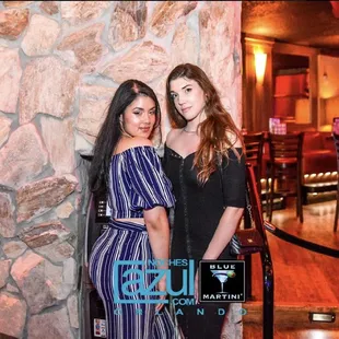 two women standing in front of a stone wall