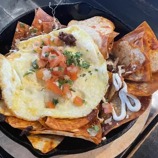 Chilaquiles with homemade tortilla chips, red sauce, beans, cheese, Mexican crema, with over-easy eggs, pico de gallo, with chorizo.