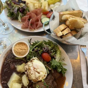 Top plate: raclette, salami, prosciutto and salad. Bottom: beef stew, yucca, rice, black bean and salad
