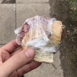 a person holding a sandwich wrapped in plastic