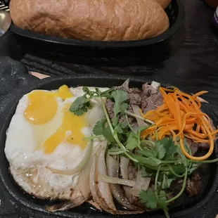 Eat breakfast the Vietnamese way! Seared steak with sunny side eggs, Banh mi, and pate. All served on a sizzling hot plate!