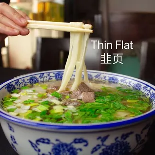 a person holding chopsticks over a bowl of soup