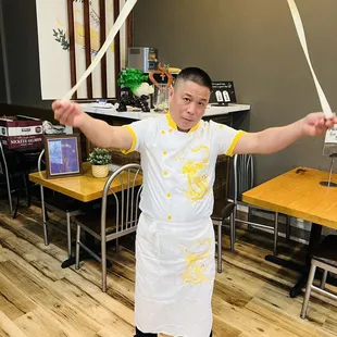 a man in a chef&apos;s apron holding a noodles wand