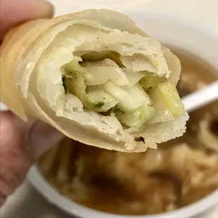 a person holding a roll with a bowl of soup in the background