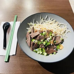 a bowl of beef and noodles with chopsticks