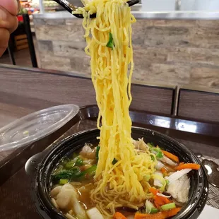 a person holding a pair of chopsticks above a bowl of noodles