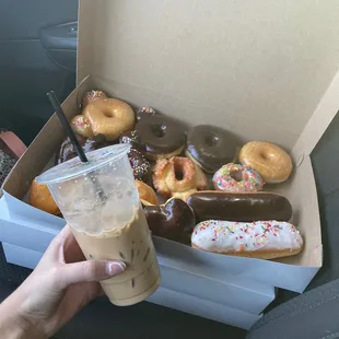 a person holding a cup of coffee and a box of donuts