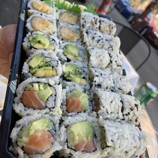 a hand holding a tray of nori sushi