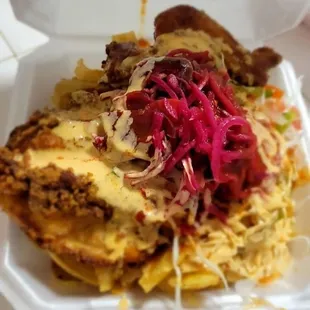 Pollo con Tajadas: Fried chicken, fried green plantain strips topped with cabbage salad, pickled onion, pico de gallo, &amp; signature sauces