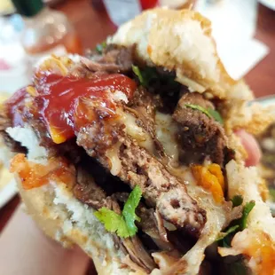 a hand holding a sandwich with meat and vegetables