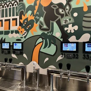 a row of beer taps in front of a colorful mural