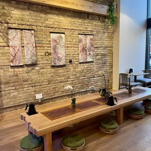 a wooden table with four green stools in front of a brick wall