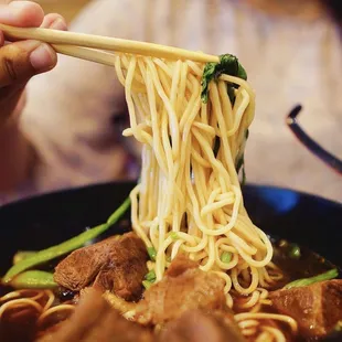a person holding chopsticks over a bowl of noodles