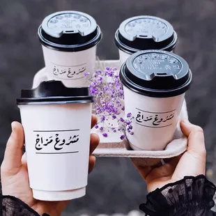 a person holding a tray with three cups of coffee