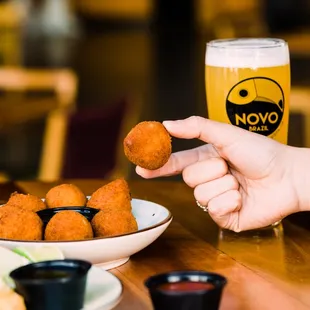 a person holding a beer and a plate of fried chicken nuggies