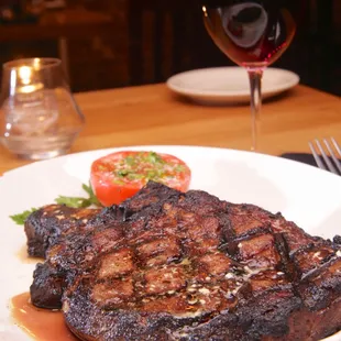  a steak on a plate with tomatoes and a glass of wine