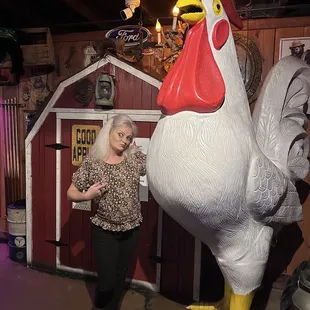 a woman standing next to a giant chicken