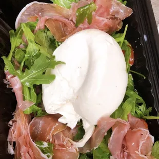 a close up of a salad with prosciutto and a dollop of