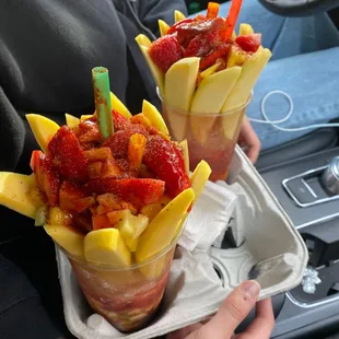 a person holding a tray of fruit cups